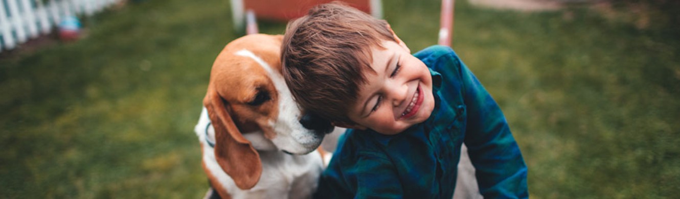 Boy laughing with his eyes shut as he plays with dog